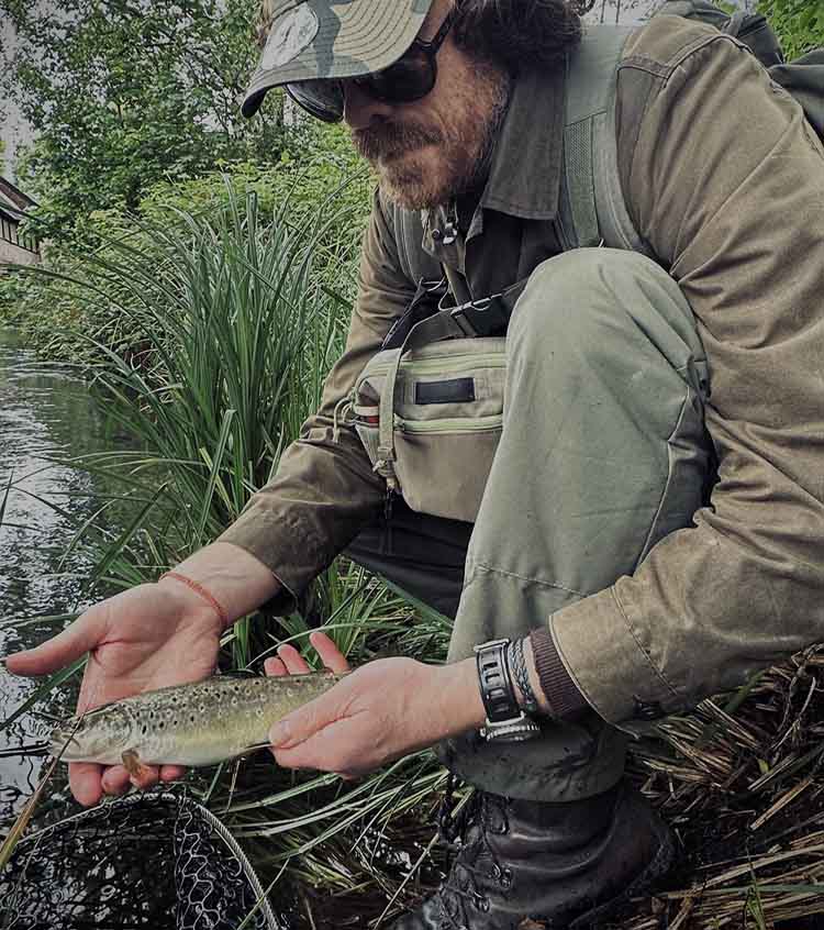 Farlows staff member RIchard fishing for brown trout Richard holding a trout by the water just out of the net before release